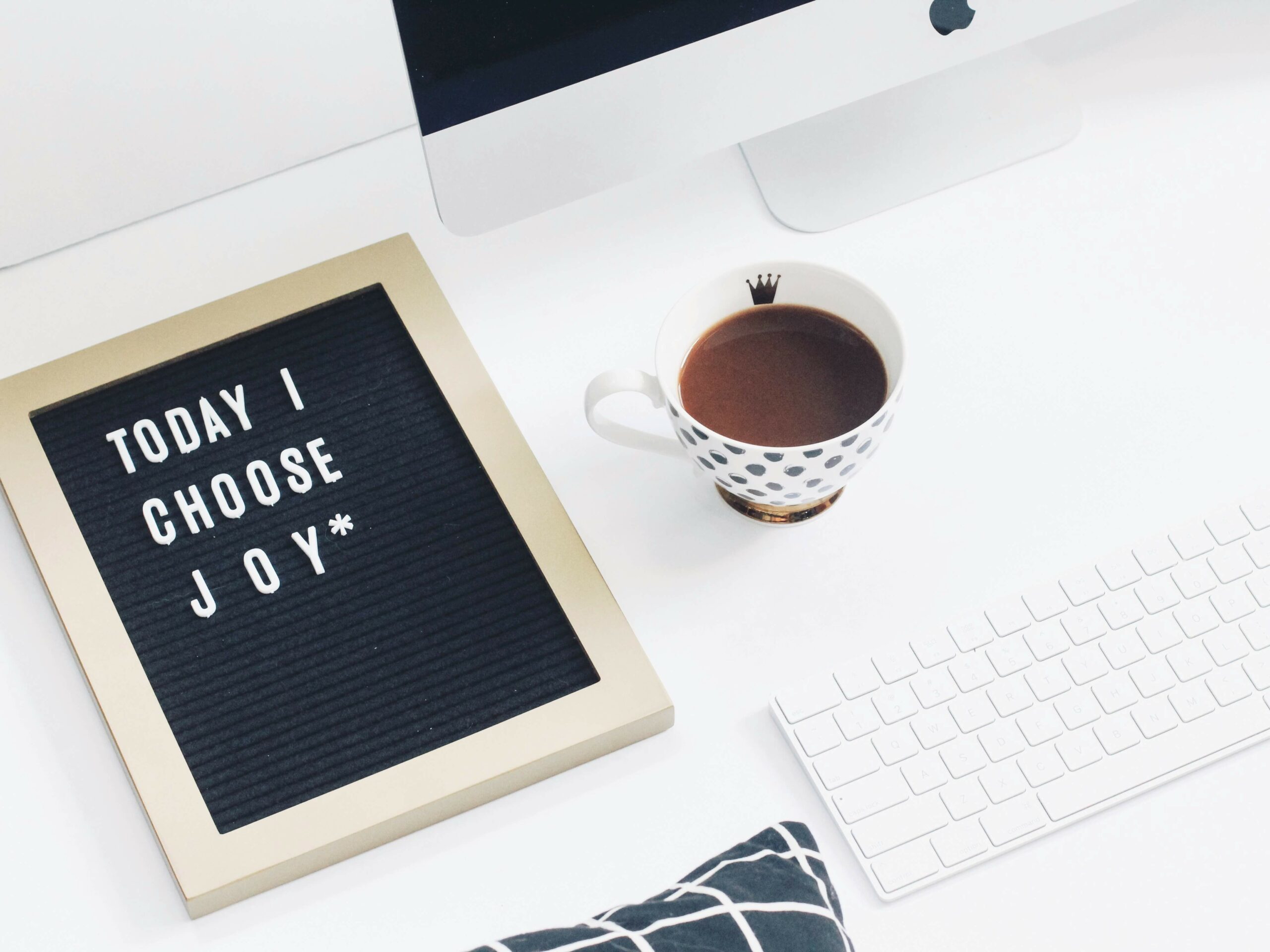 Image of a corkboard with the words "today I choose joy*" and a coffee cup and computer on a white desk